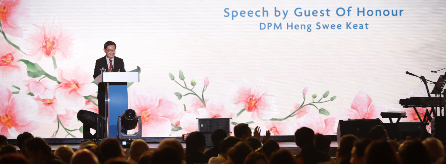 DPM Heng Swee Keat speaks on stage before a floral backdrop to an audience.